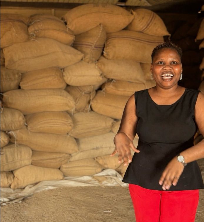 Oluwaseun Lijoka smiling in front of stacked jute sacks in a warehouse